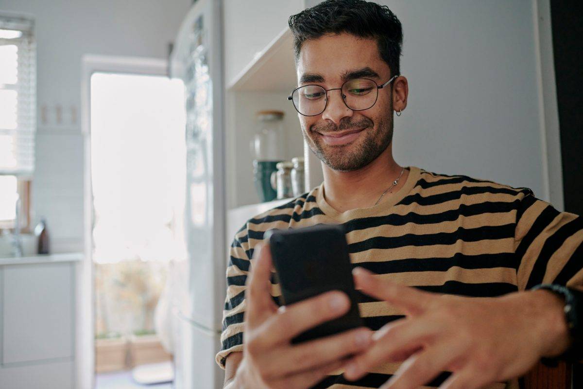 A man smiling at his phone in his kitchen